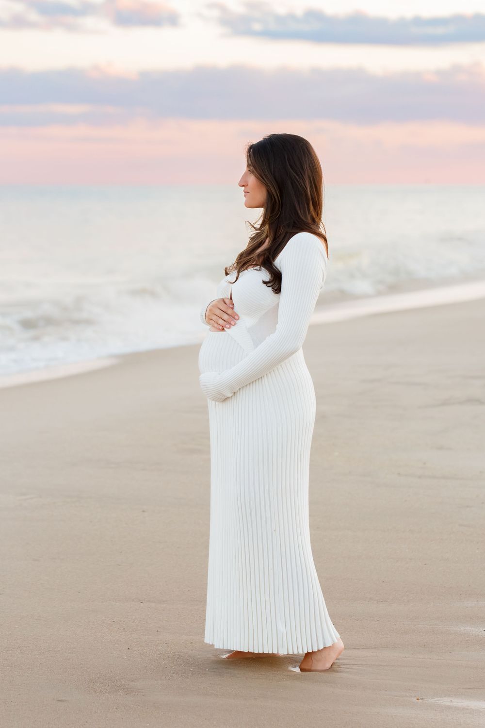 A person in a flowing white dress stands on a sandy beach at sunset in a series of maternity photos.