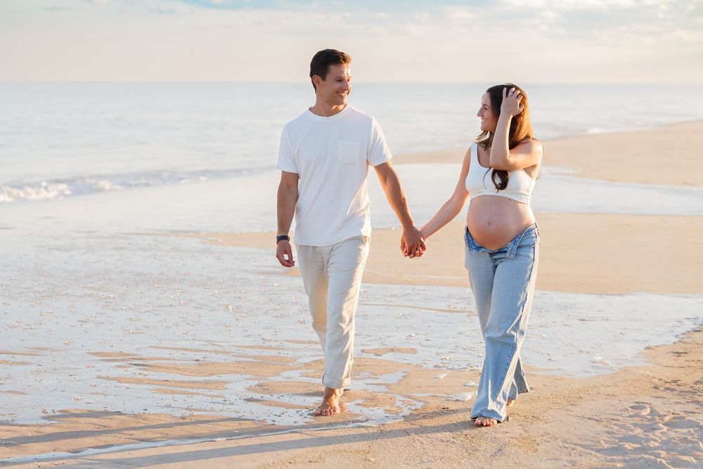Couple walking hand in hand along a sandy beach at sunset with ocean waves rolling in.