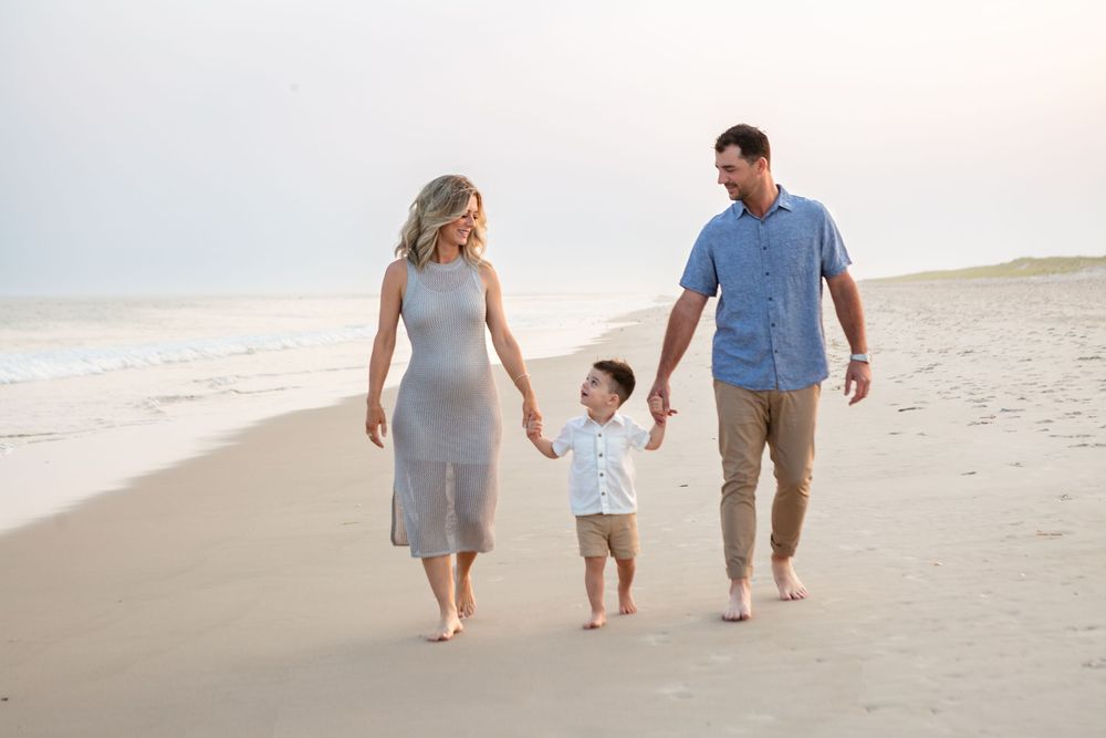 Family in coordinating gray and blue outfits walking together on a sandy beach at sunset.