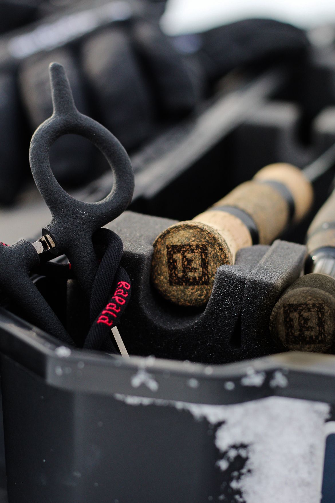 Black fishing gear components and cork handles arranged in a storage case.