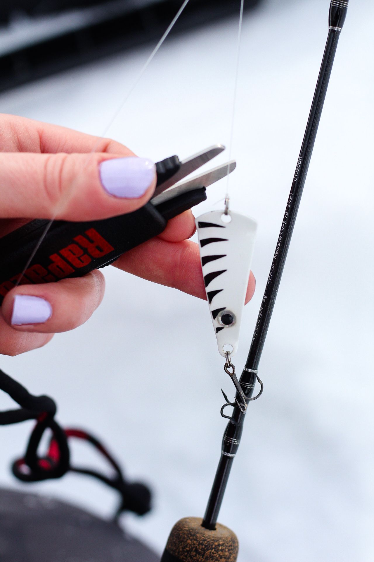 Close-up of fishing lure attachments being secured to a fishing line against a white background.