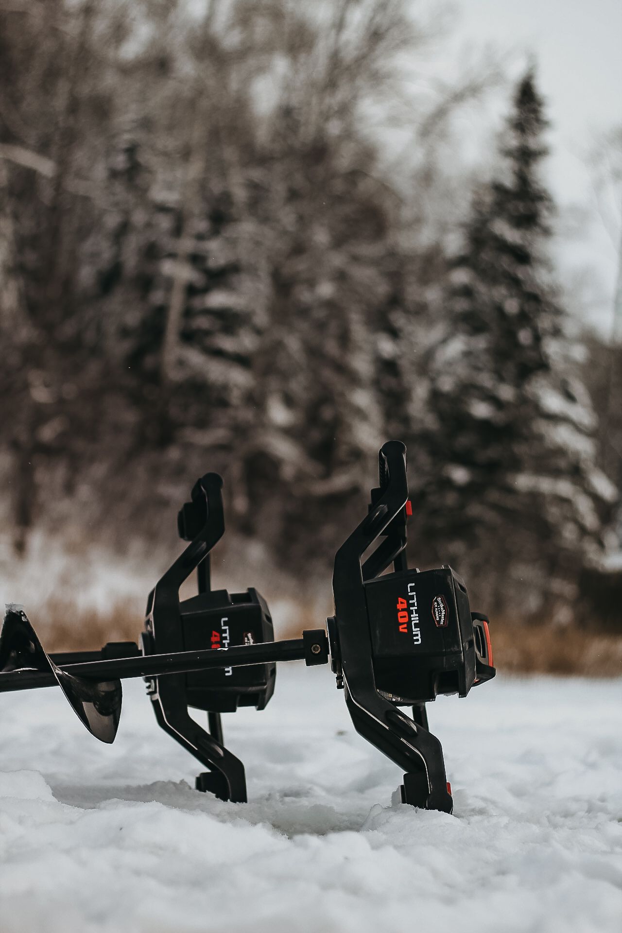 Row of black fishing reels displayed in snow with winter trees in background.