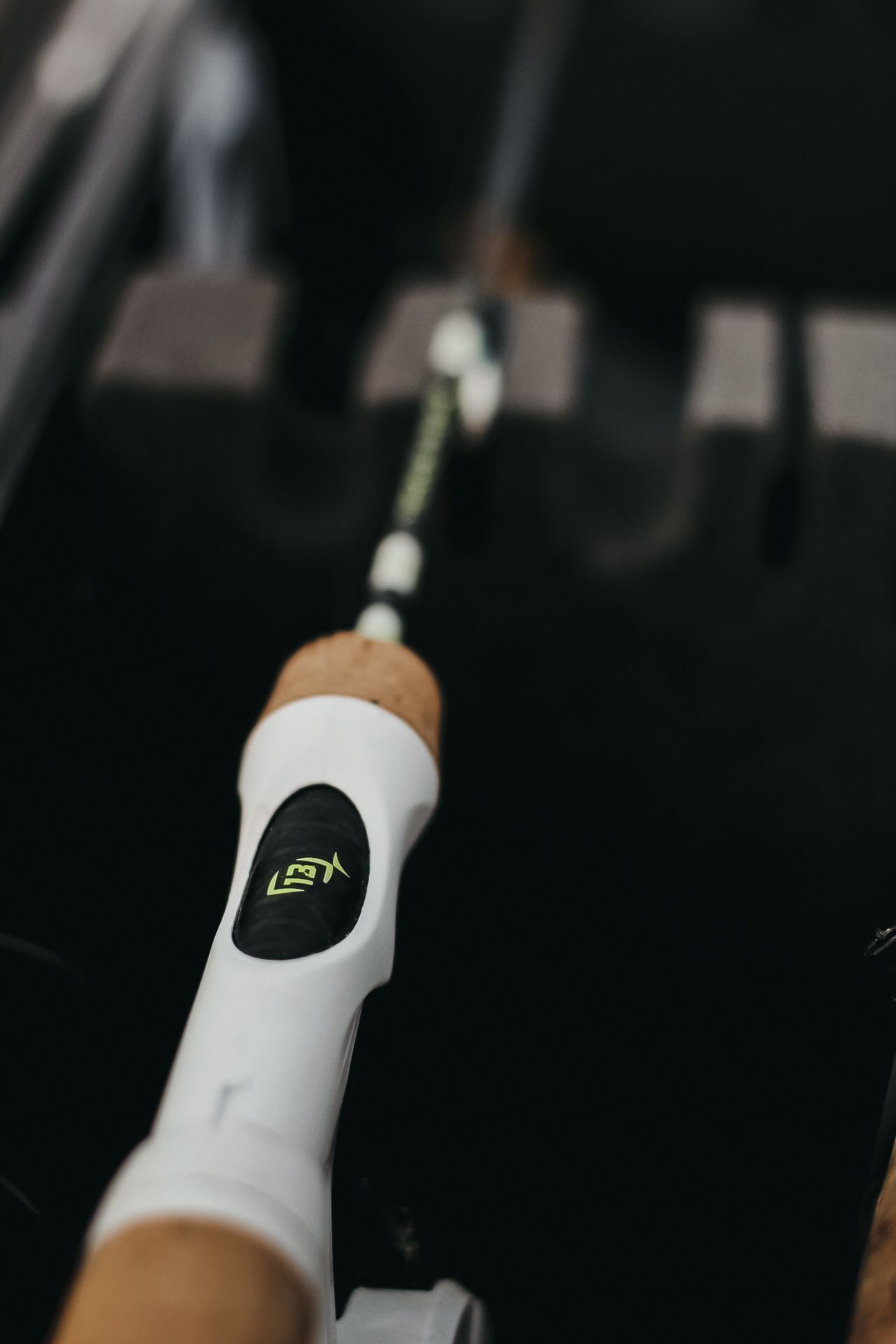 White fishing rod handle with logo detail photographed against dark background.