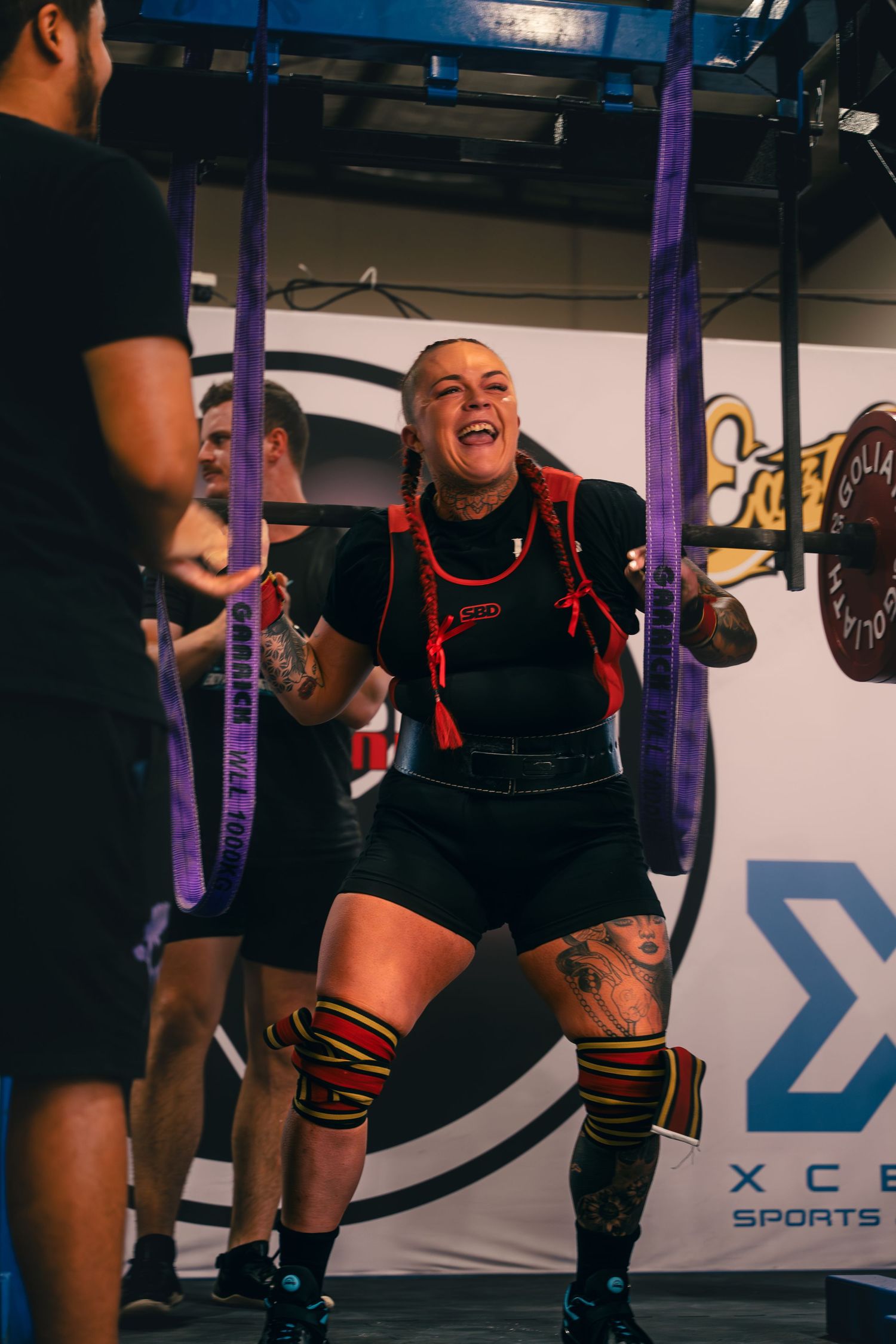 Weightlifter in black attire performing squat exercise with purple support bands.