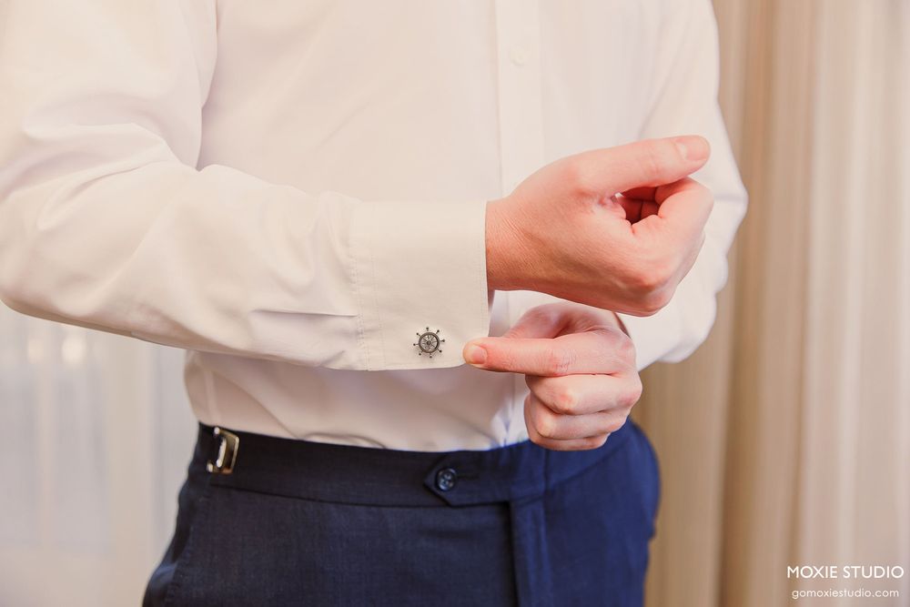 Close-up view of hands adjusting silver cufflinks on a white dress shirt sleeve.