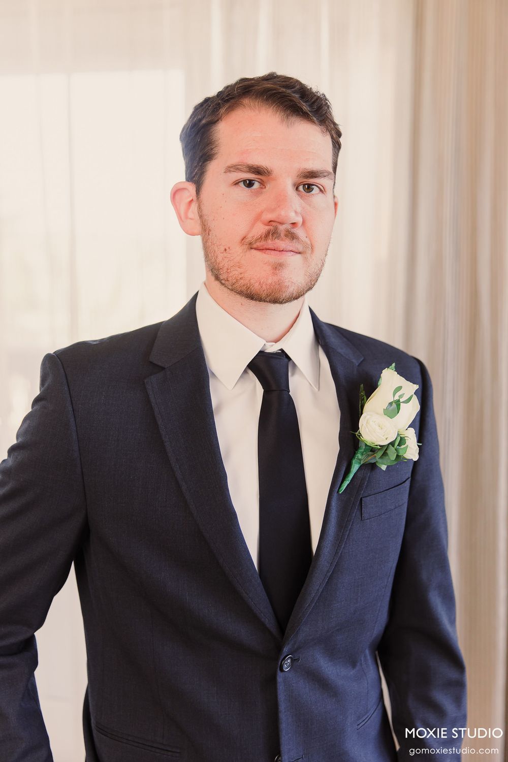 Four sequential photos showing a groom in a dark suit with white boutonniere smiling in a formal wedding portrait setting.