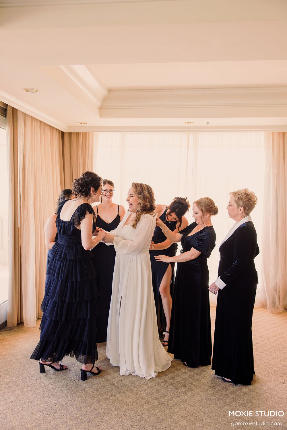 A sequence of wedding party photos showing people in navy blue and white dresses hugging in a bright hotel room.