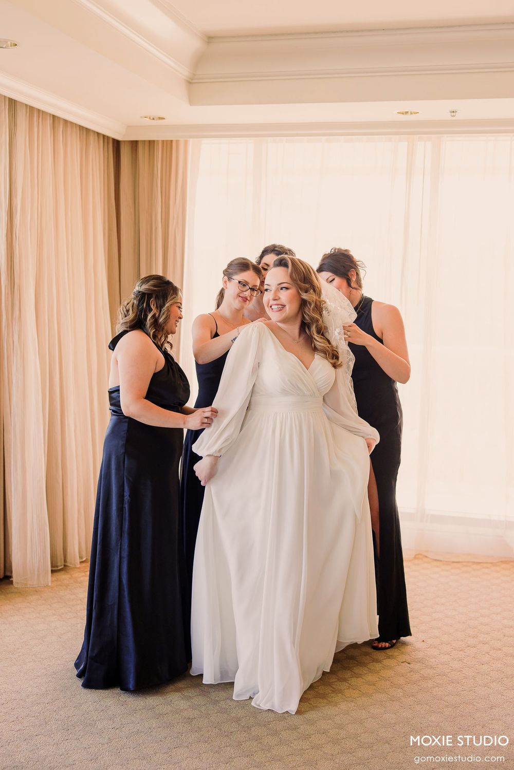 A series of photos showing bridesmaids in navy dresses helping with final wedding dress preparations in a bright room.