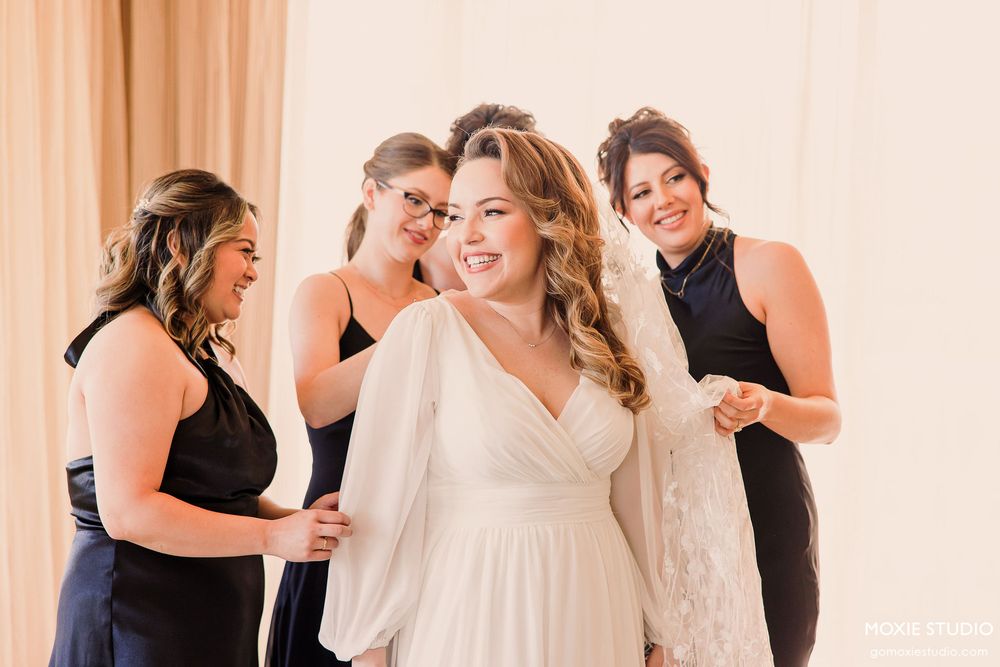 Wedding party members share joyful candid moments while getting ready in a bright indoor space.