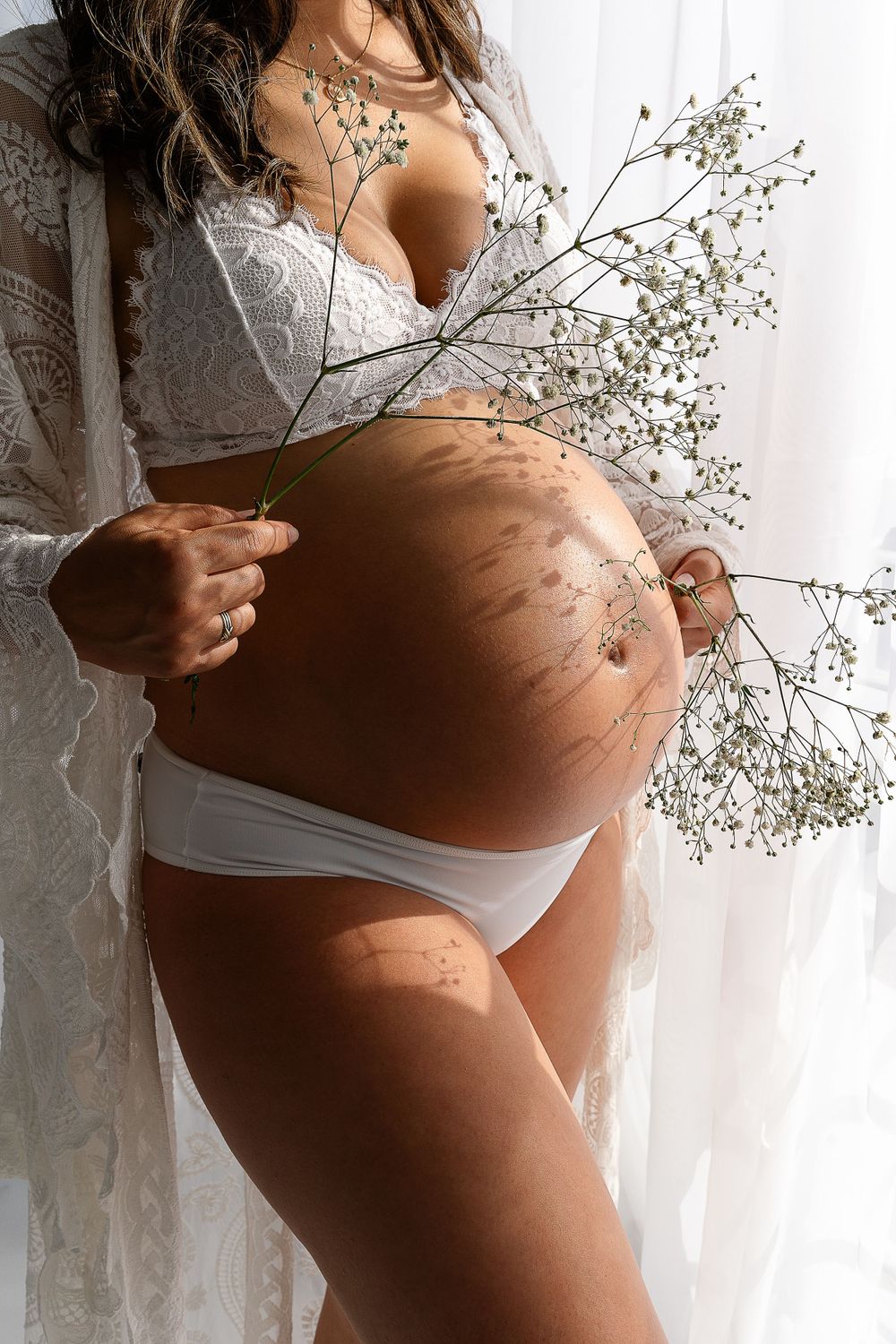 Maternity photo showing pregnant belly with baby's breath flowers against white backdrop.