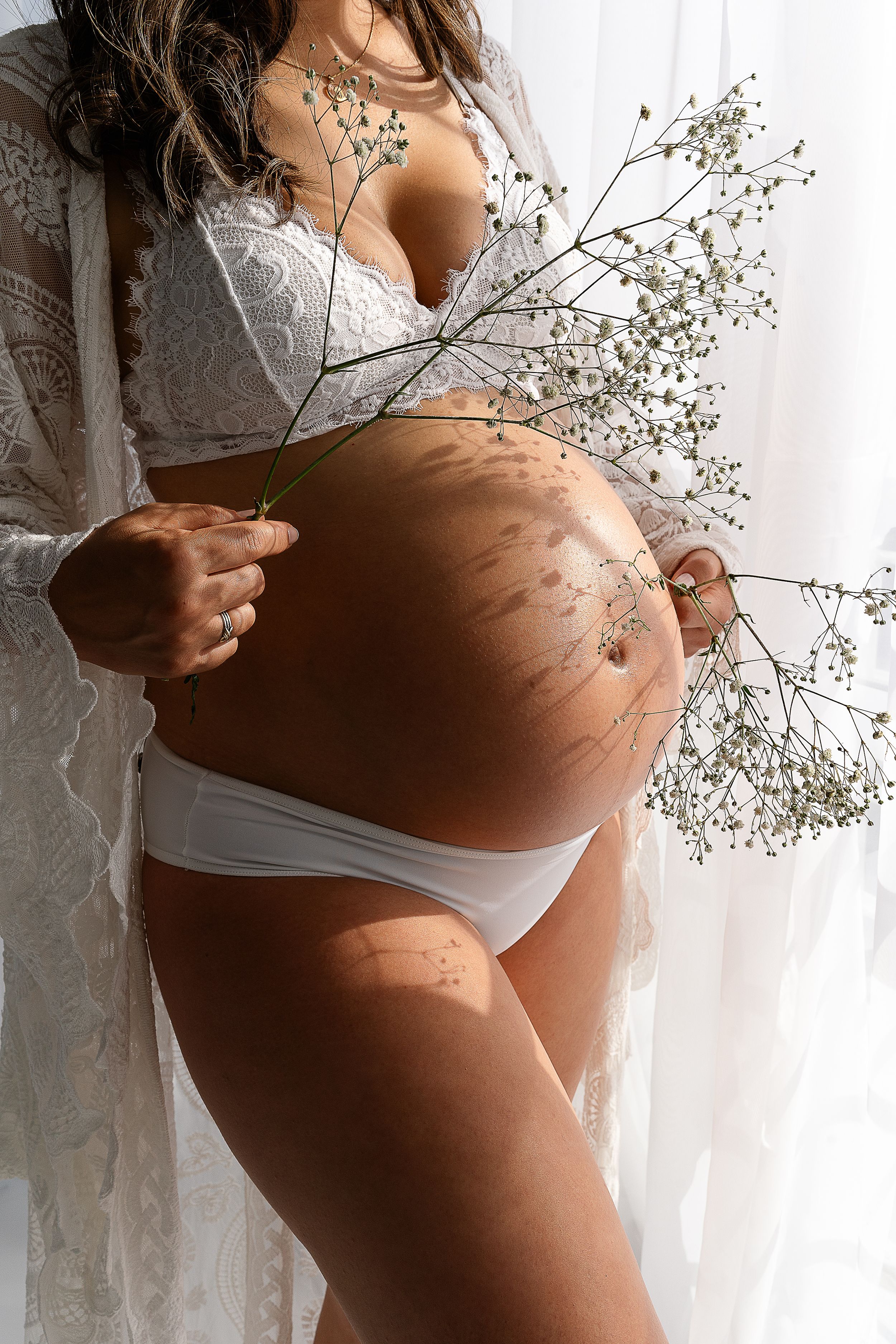 Maternity photo showing pregnant belly with baby's breath flowers against white backdrop.