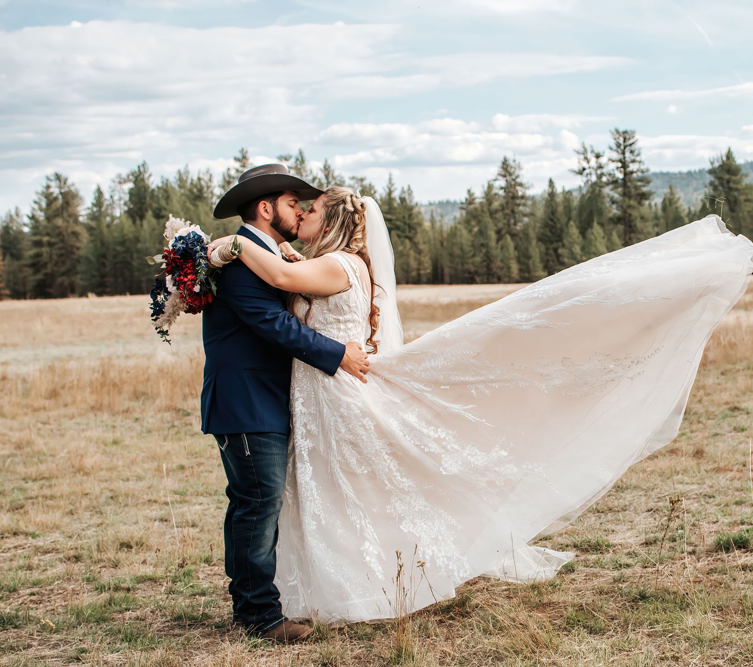 A romantic wedding couple embraces in a field with mountains and evergreen trees in the background in Oregon.