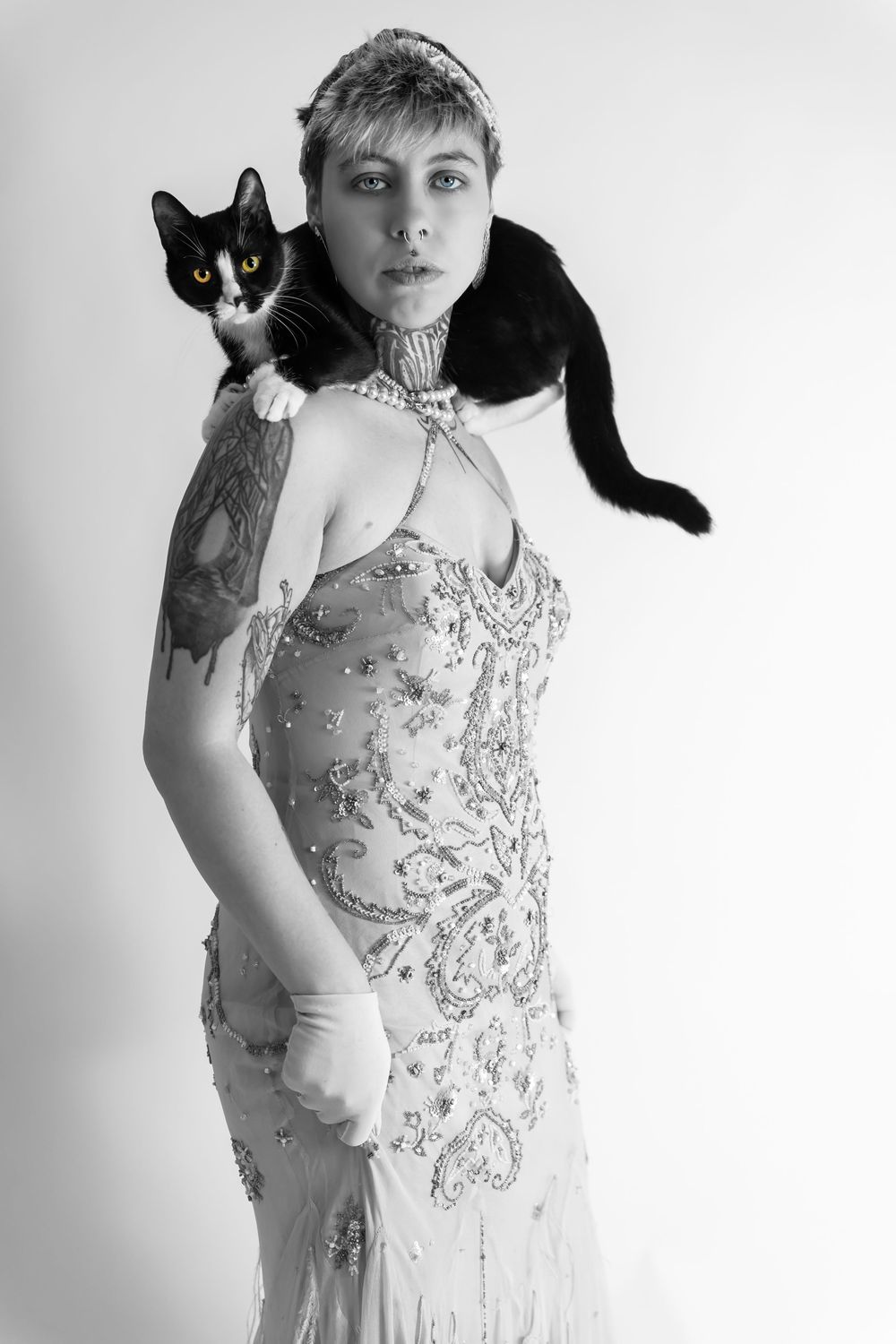 Black and white photo of woman in beaded flapper dress with tuxedo cat on her shoulder.