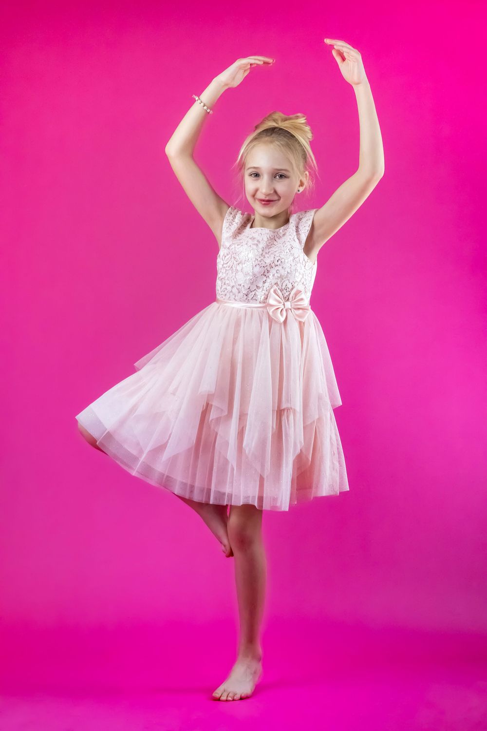 Dancing figure in pink tulle dress captured in motion against vibrant pink background.