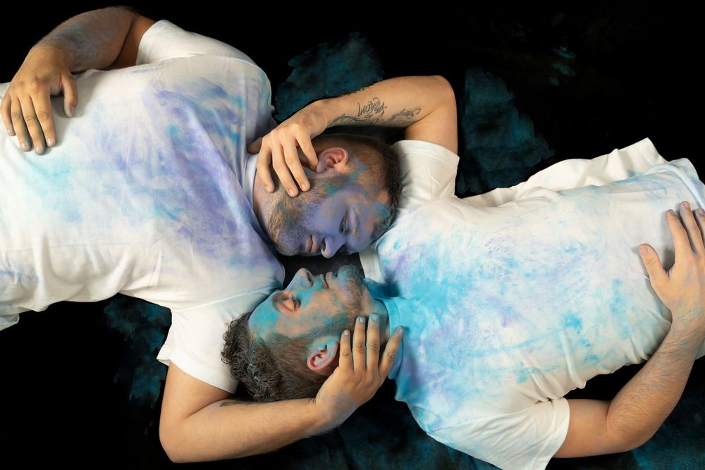 Two people lying down surrounded by ethereal blue powder effect against black backdrop.
