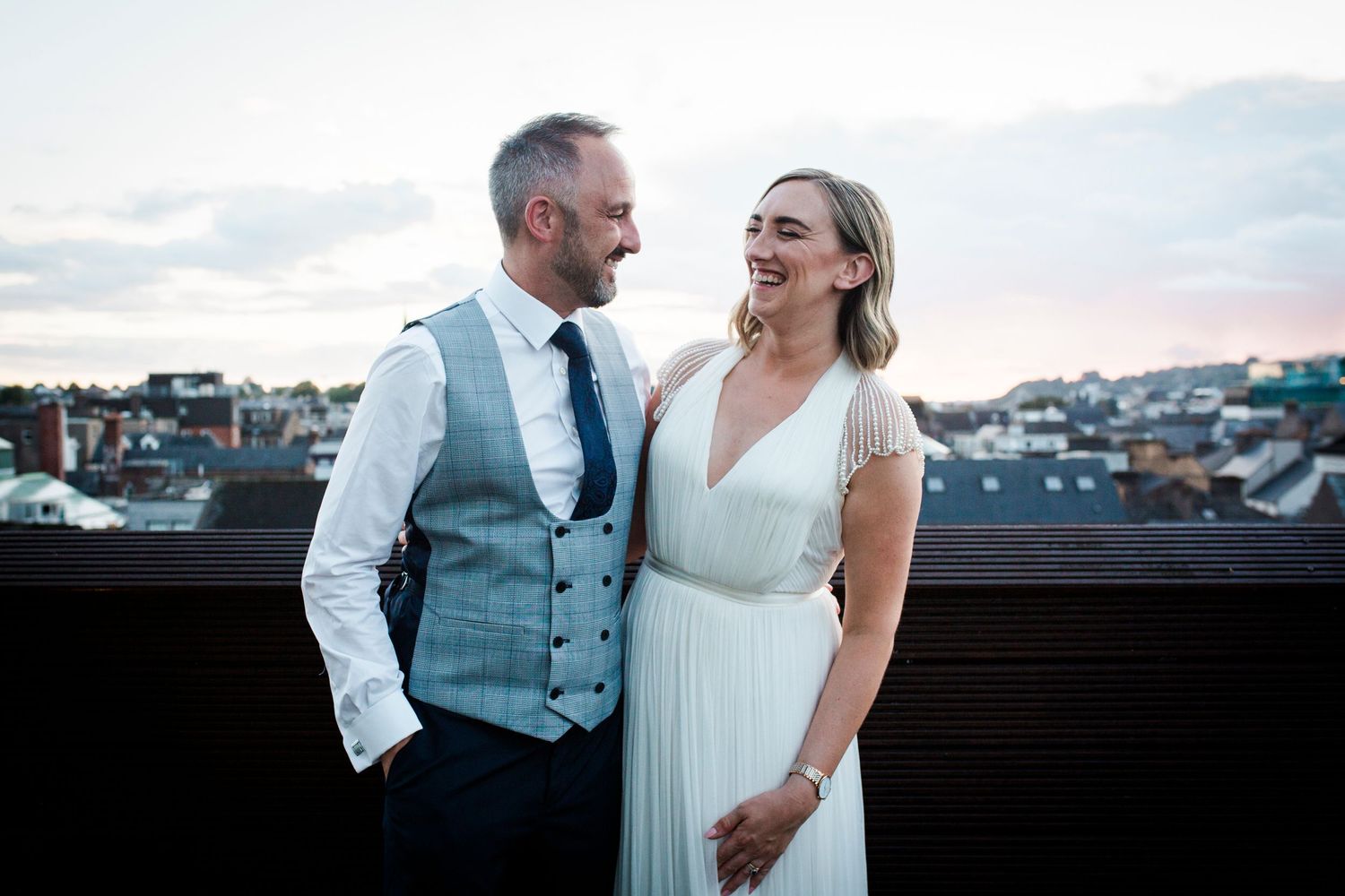 Romantic rooftop moment at sunset with city skyline in background.