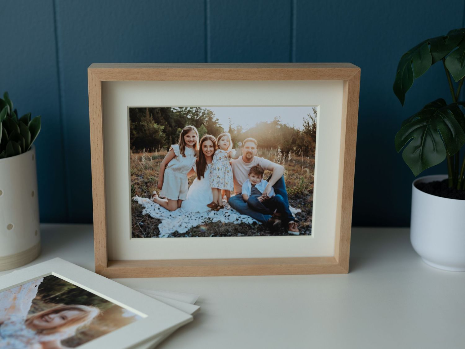 Framed family portrait displayed on white desk with houseplants and decor.