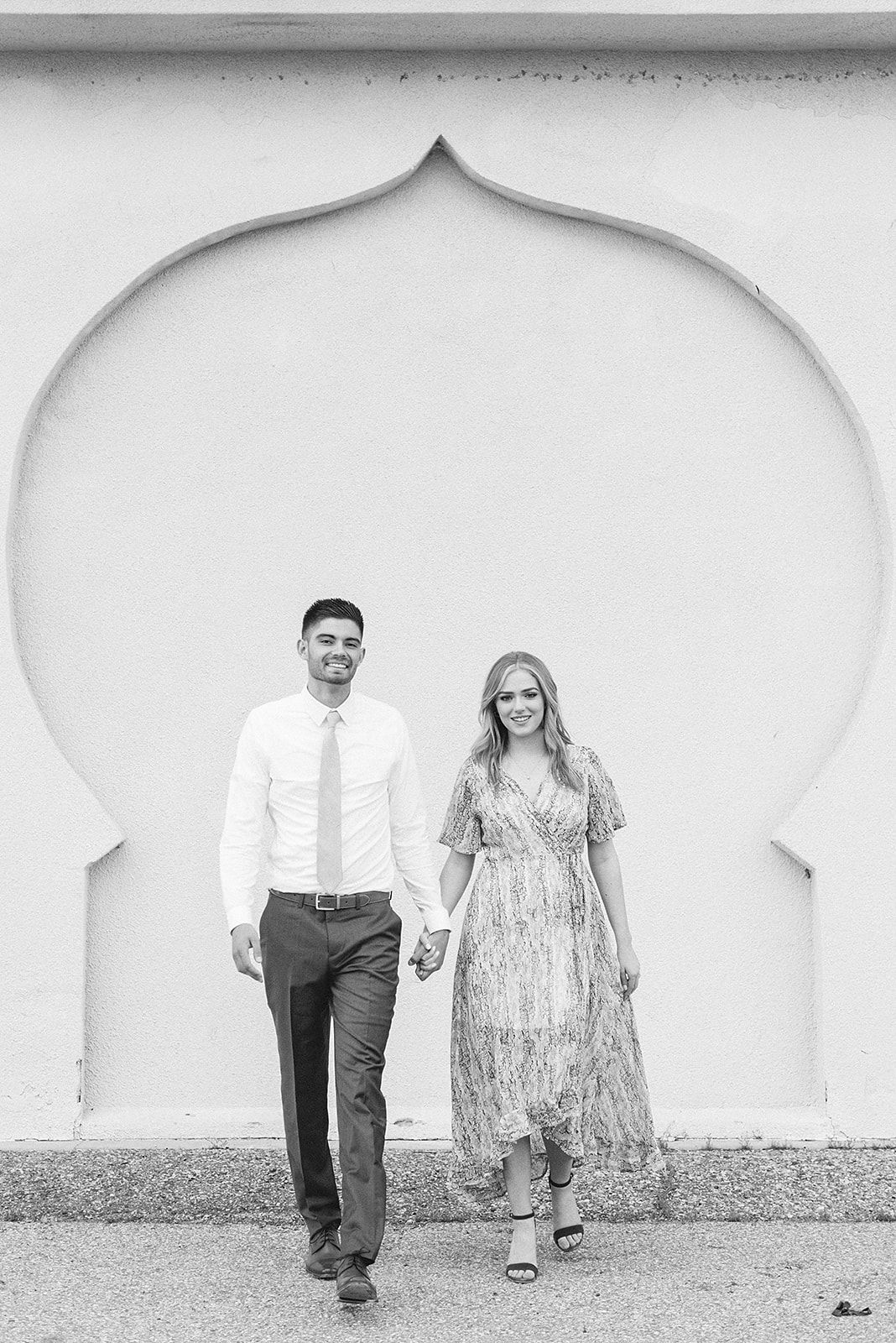 A couple stands together in a white archway wearing formal attire.