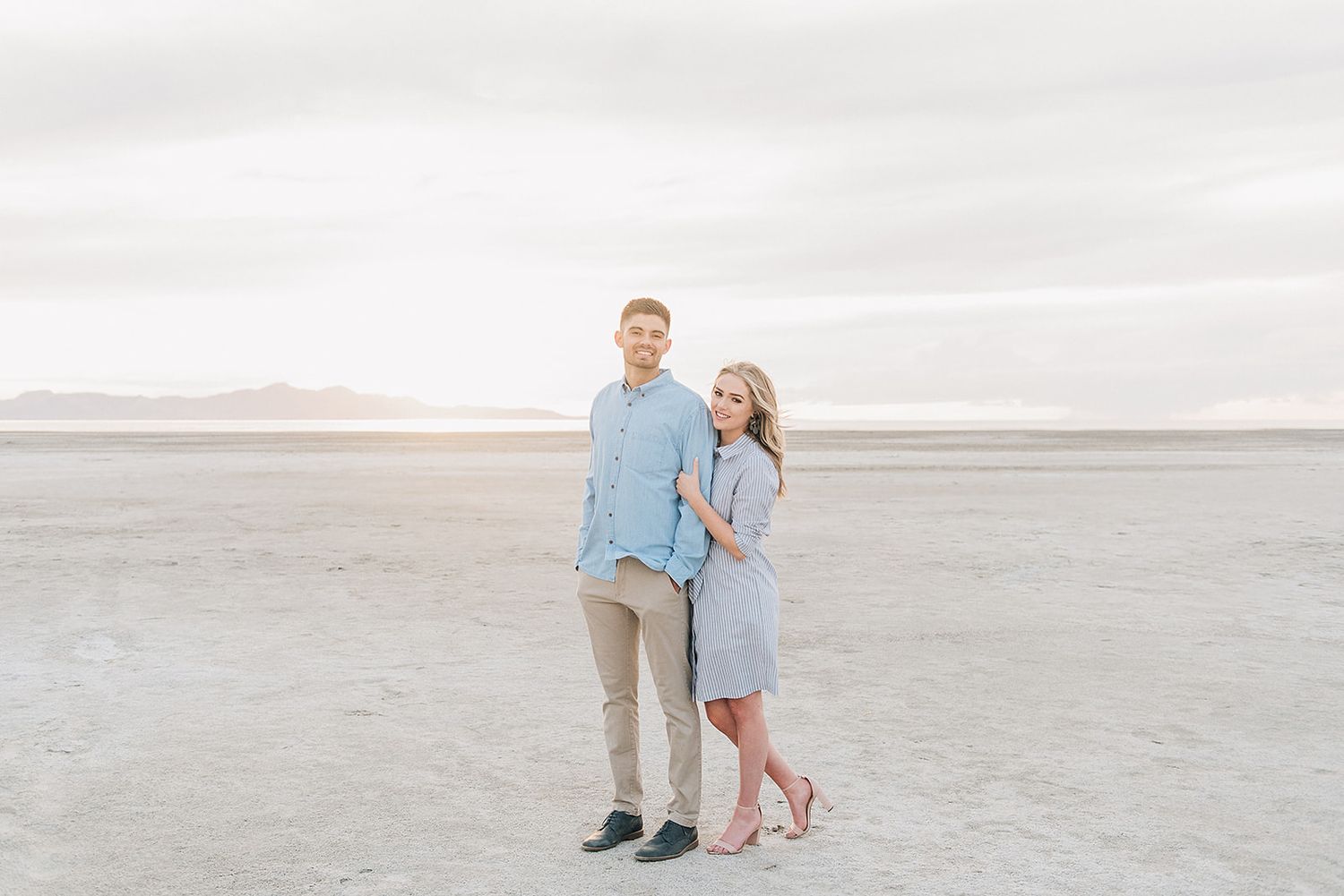 A romantic couple poses on a salt flat desert landscape during golden hour.