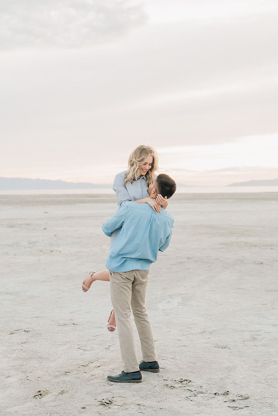 A romantic moment captured as a couple shares a playful lift on a desert salt flat.