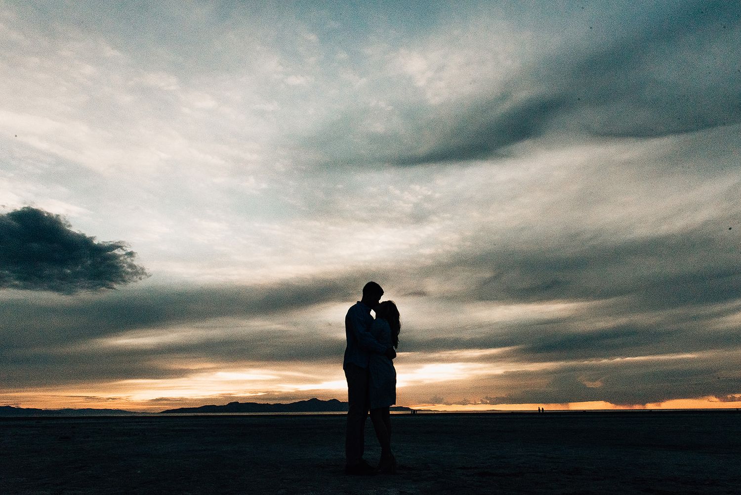 A silhouetted couple embraces against a dramatic sunset sky.