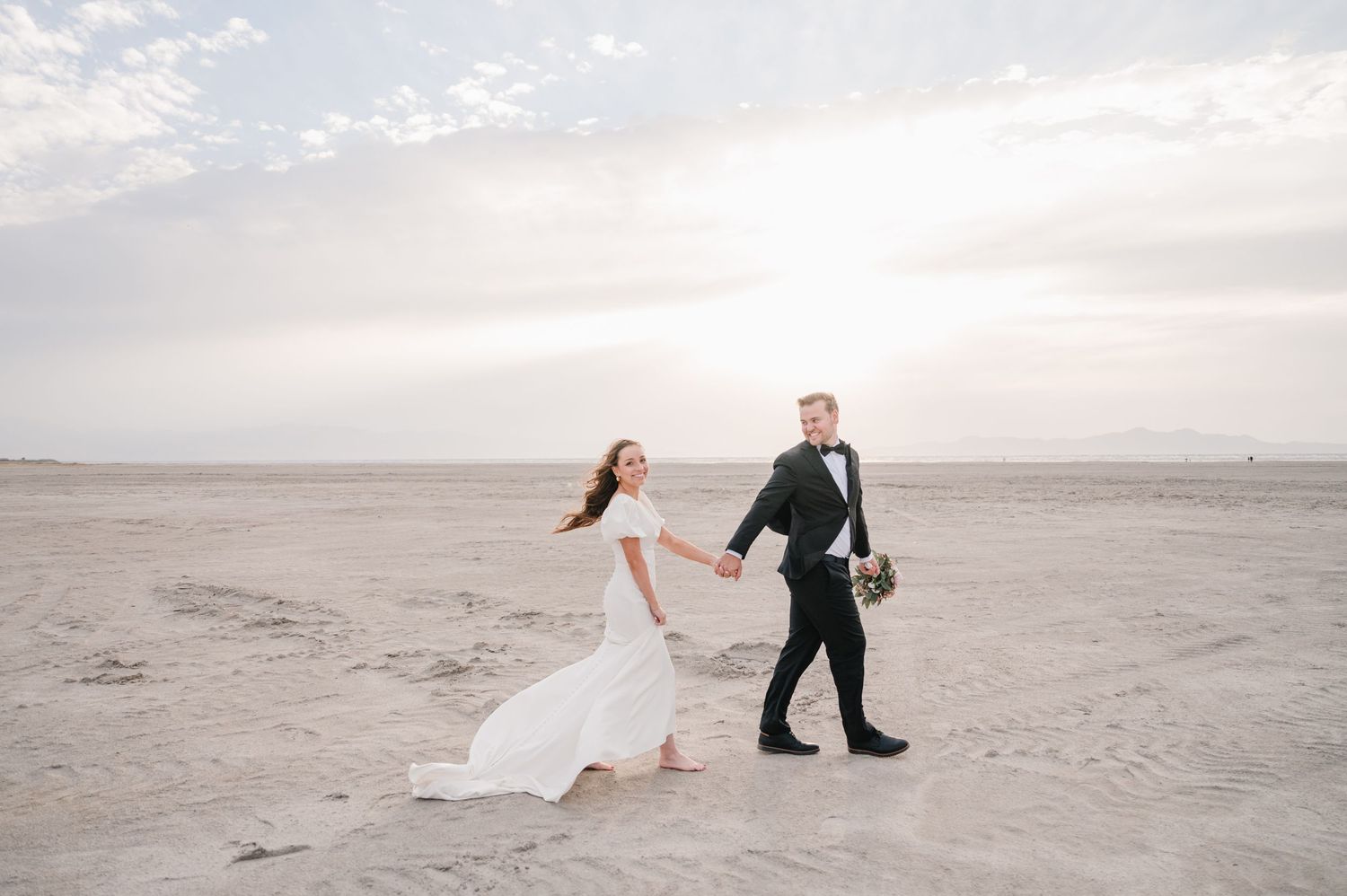 Bride and groom walking hand in hand across desert landscape with flowing white dress.