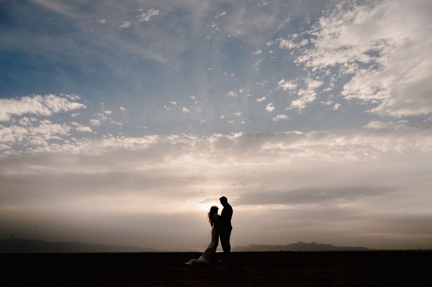 Silhouette of couple standing together against dramatic cloudy sunset sky.