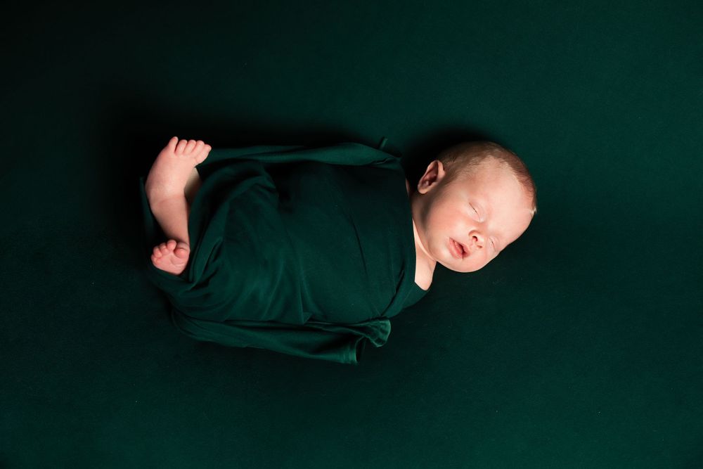 Newborn baby wrapped in dark green fabric sleeping peacefully during studio photography session.