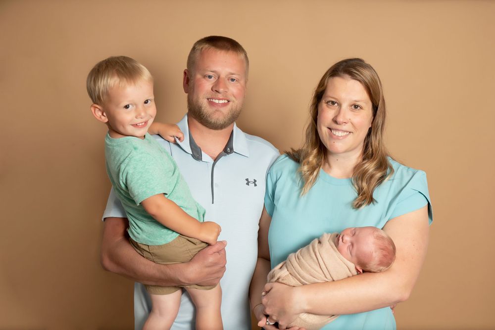 Family of four wearing coordinating blue and mint outfits pose together against brown backdrop.
