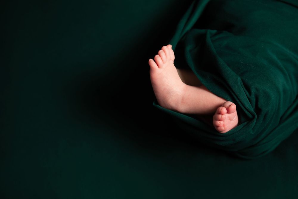Small baby feet peek out from dark green fabric against black background.