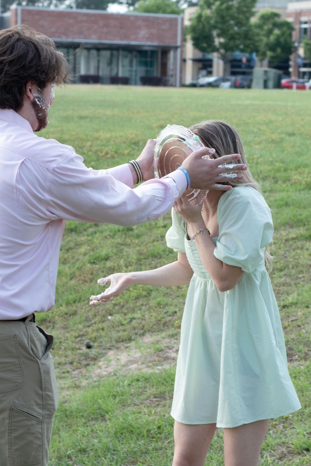 A playful moment outdoors with cake being smeared during a celebration.