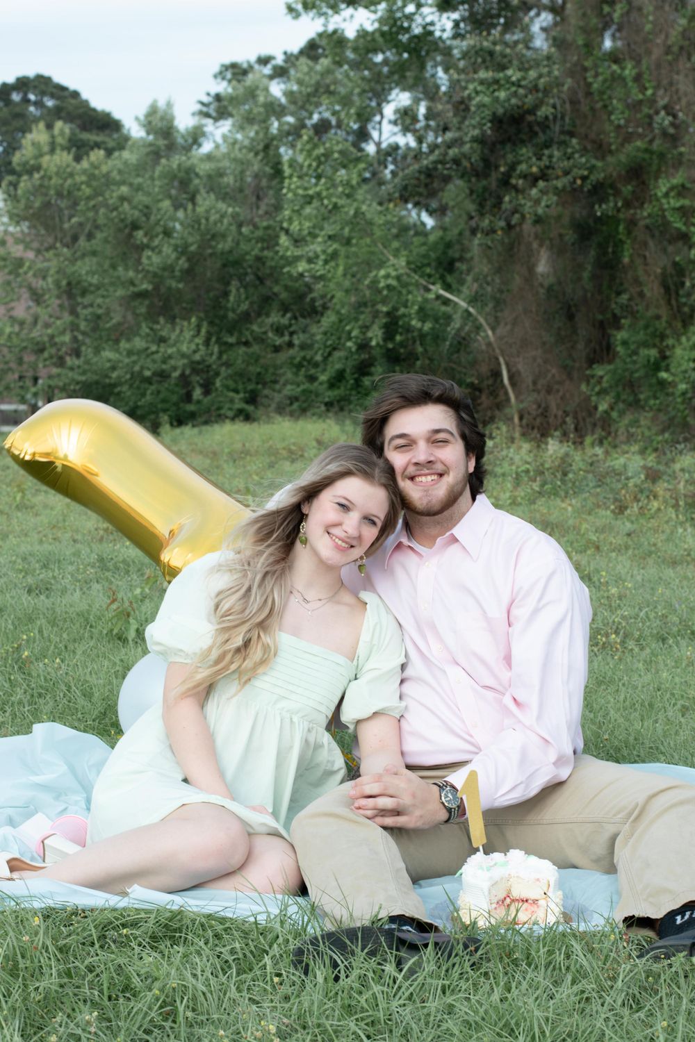 A picnic scene with balloons and cake on a blanket by a lake.