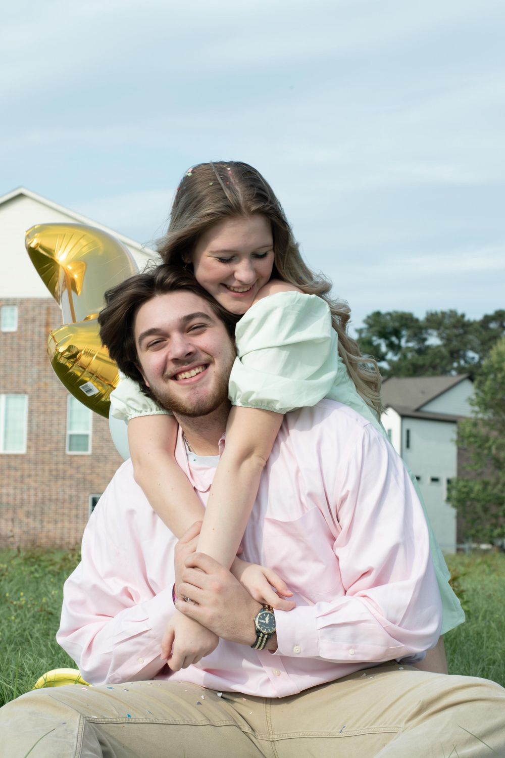 A joyful embrace during an outdoor celebration with gold balloons in the background.