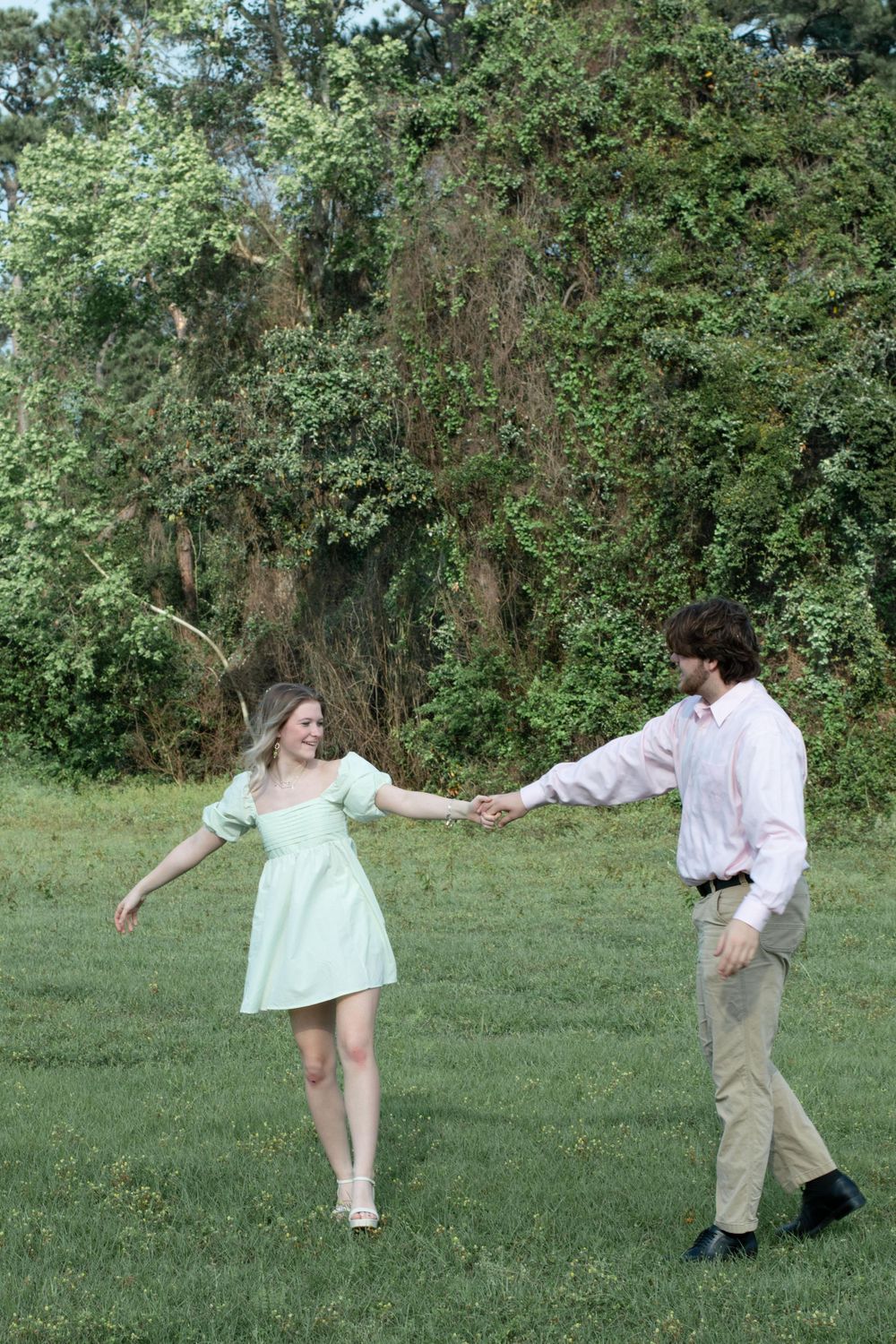 Couple dancing in green field wearing pastel outfits.