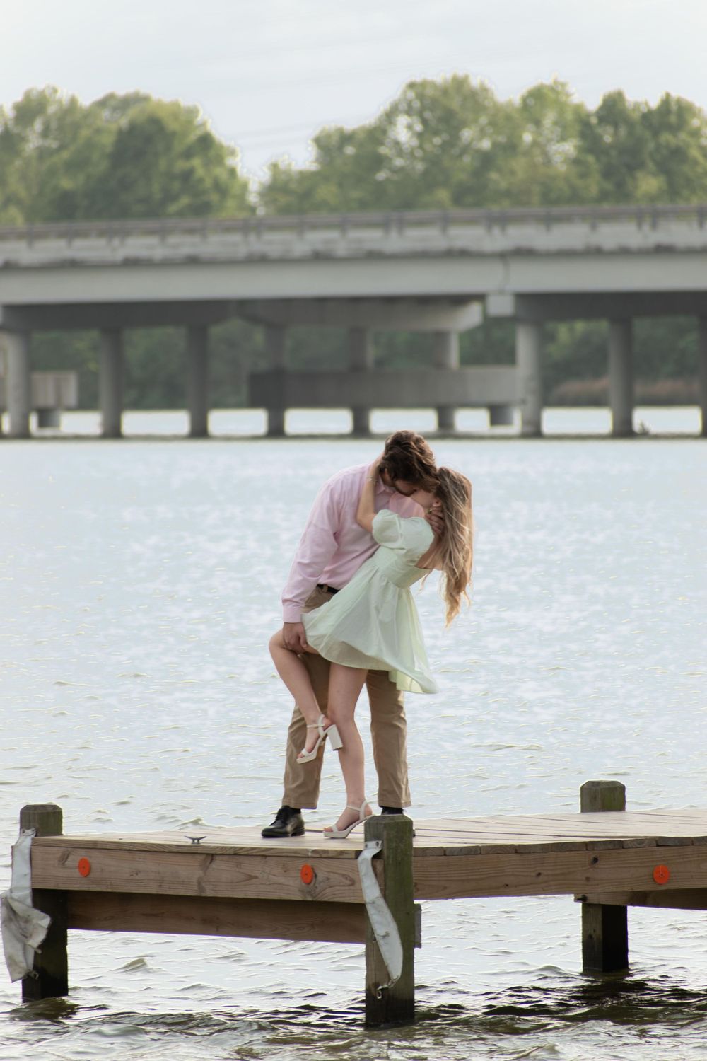 Romantic moment on wooden dock over lake with bridge in background.