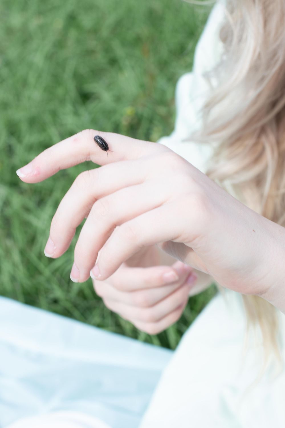 A close-up of a hand with a single black ladybug crawling on pale skin against a green background.