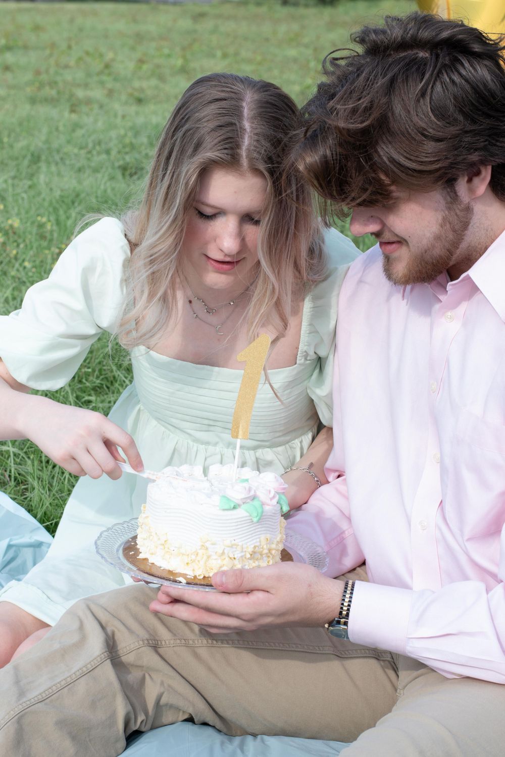 A romantic picnic scene with a couple enjoying birthday cake together on the grass.