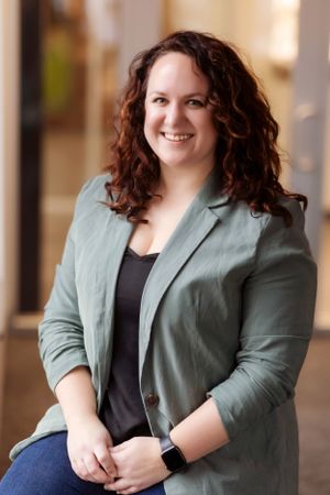 Professional portrait in office hallway wearing sage green blazer.
