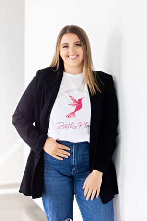 Casual business portrait wearing black blazer and pink hummingbird t-shirt.