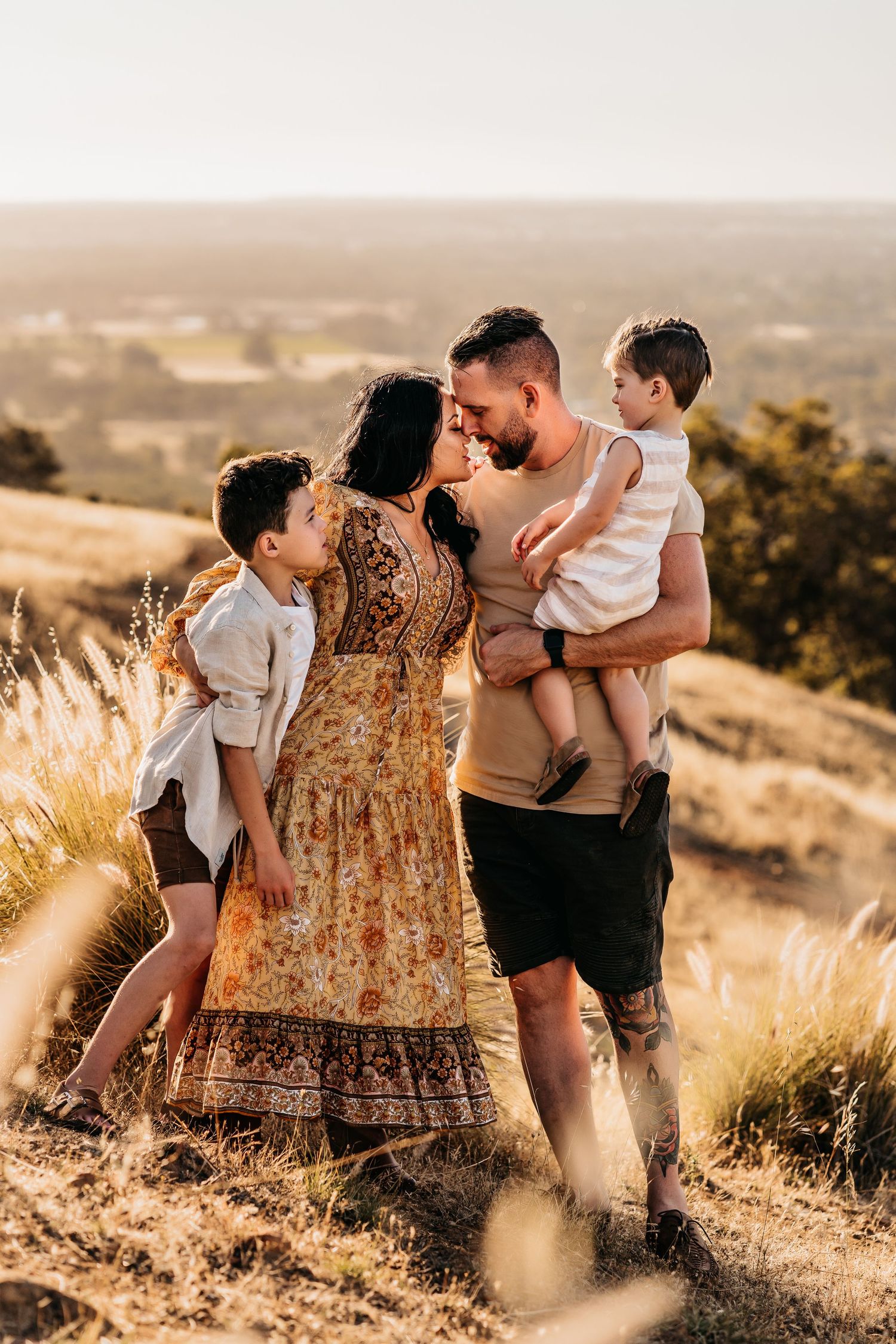 A loving family moment captured in golden light on a grassy hillside.
