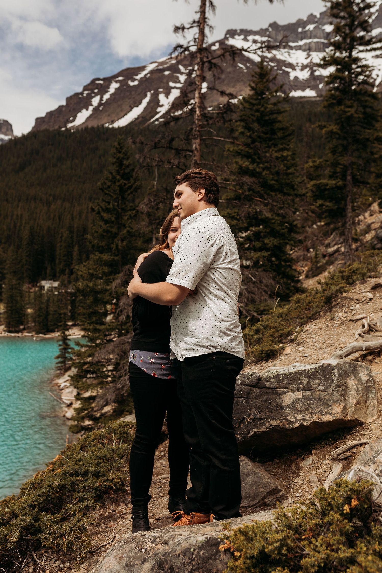 A romantic embrace against a backdrop of snow-capped mountains and turquoise lake in the wilderness.