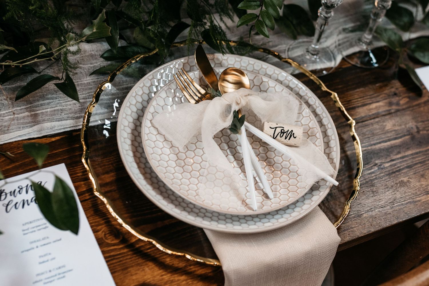 Wedding place setting with gold flatware, white napkin and lace-patterned plates on wooden table.