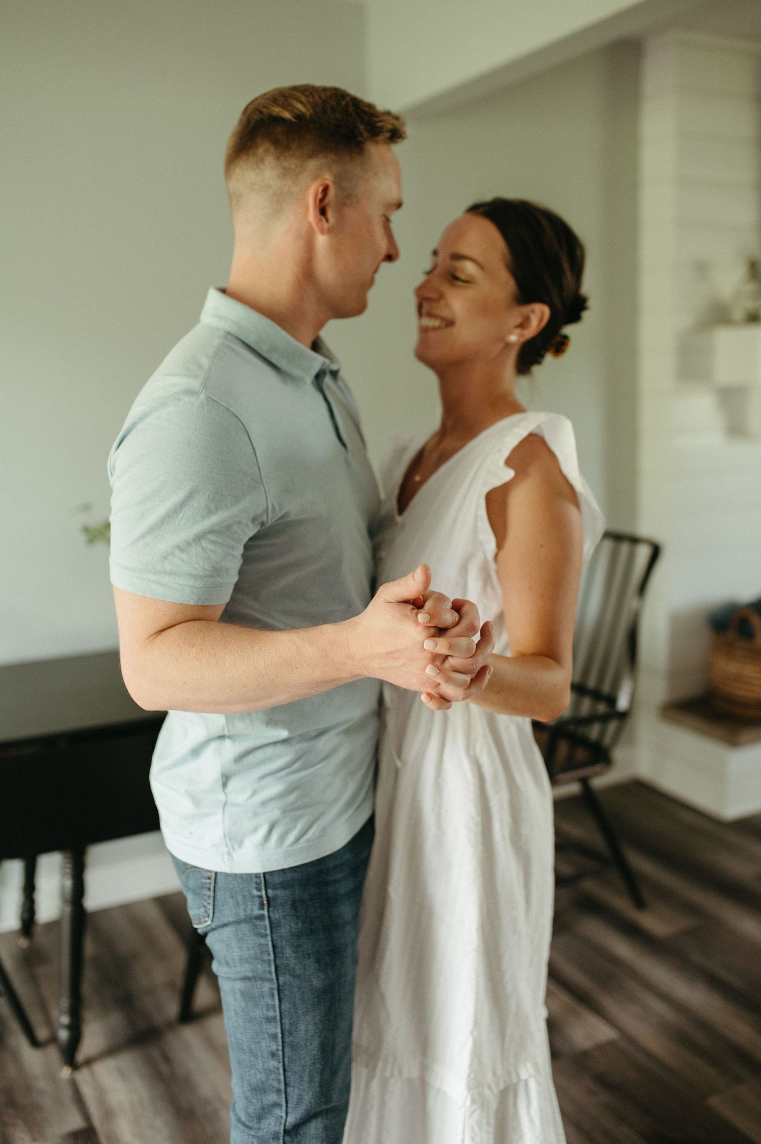 A couple holds hands and shares an intimate moment while standing in their living room.