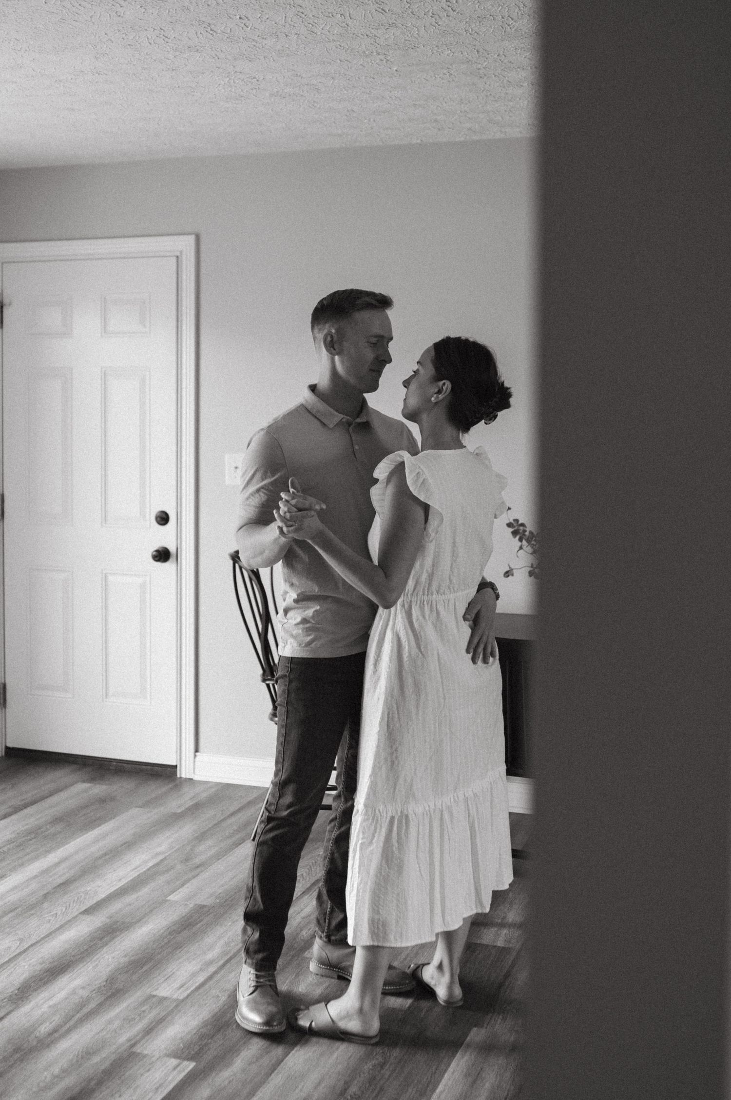 A black and white image of a couple dancing together in their home.