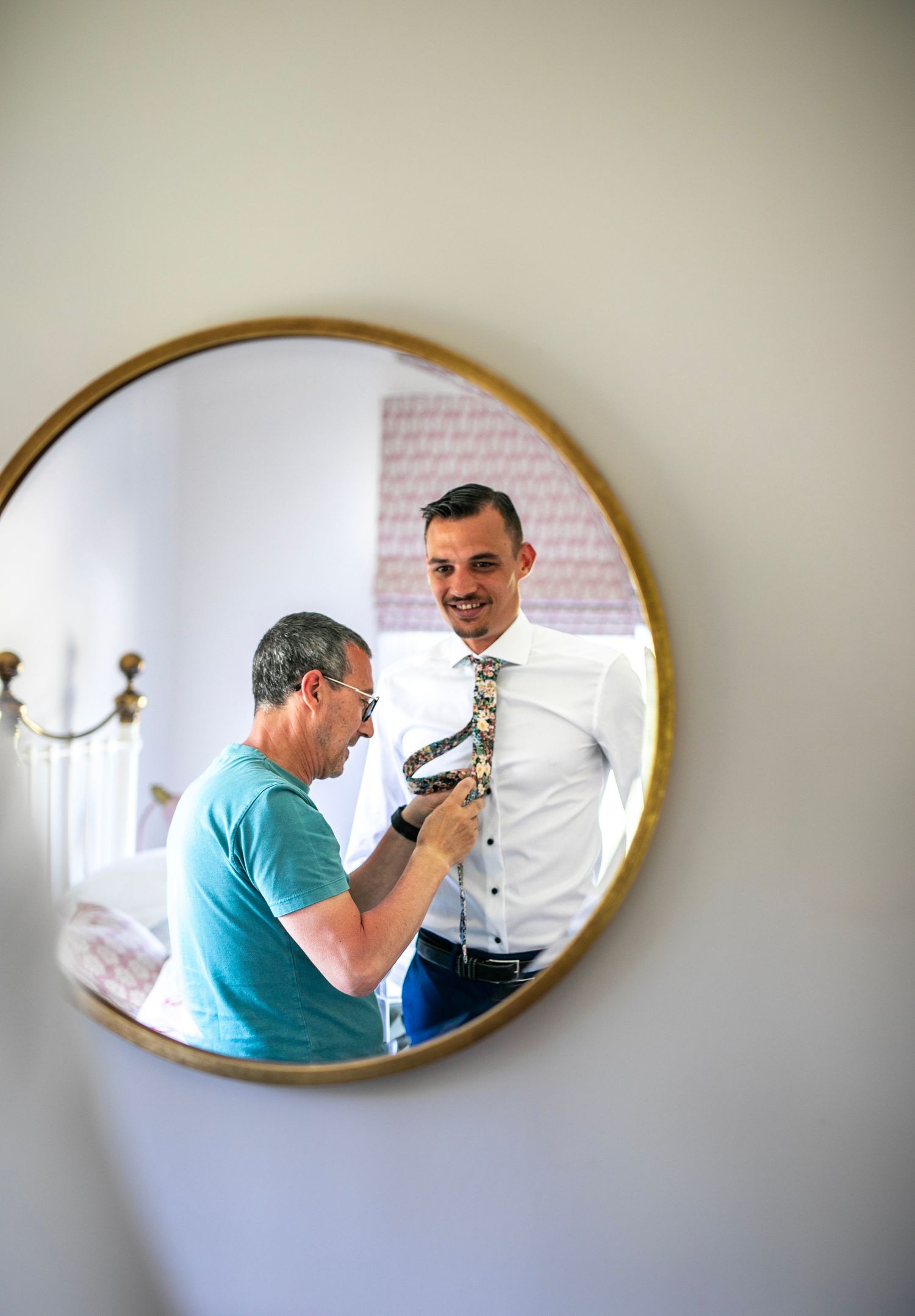 Getting ready for the wedding ceremony reflected in an oval mirror mounted on a white wall.