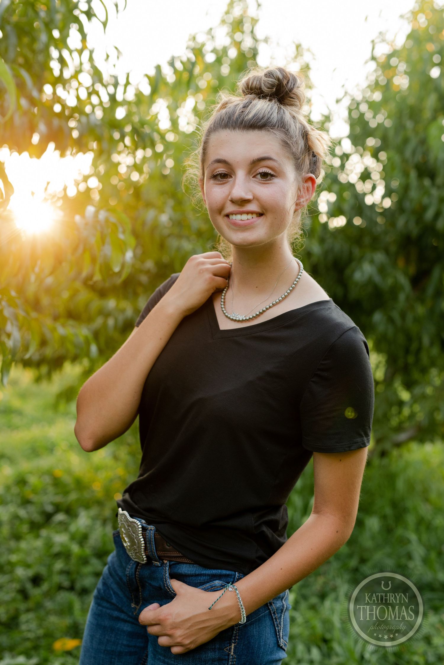 Sunset portrait in a peach orchard wearing black v-neck tee and decorative belt.