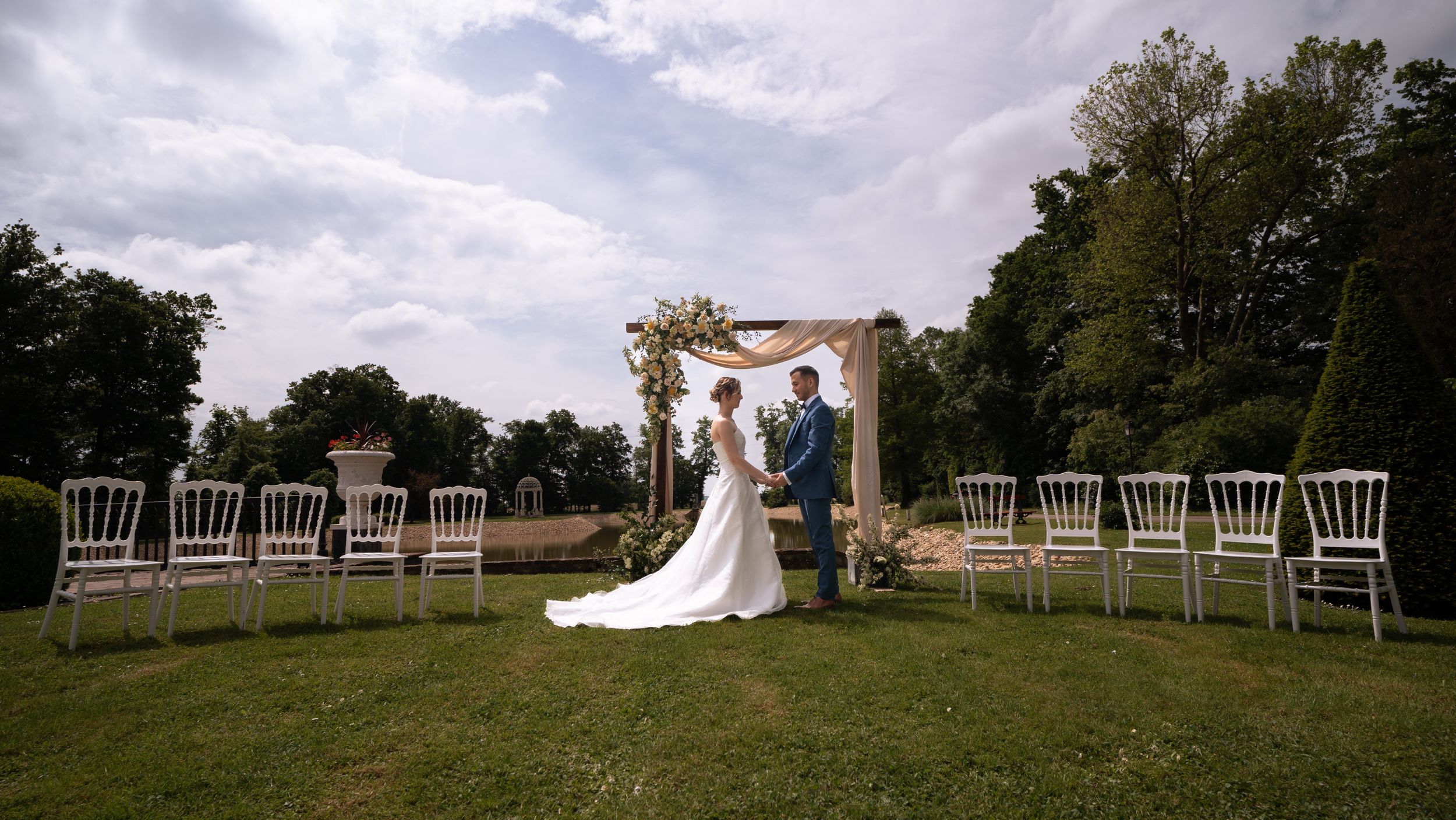 Outdoor wedding ceremony setup with white chairs and natural landscape backdrop.