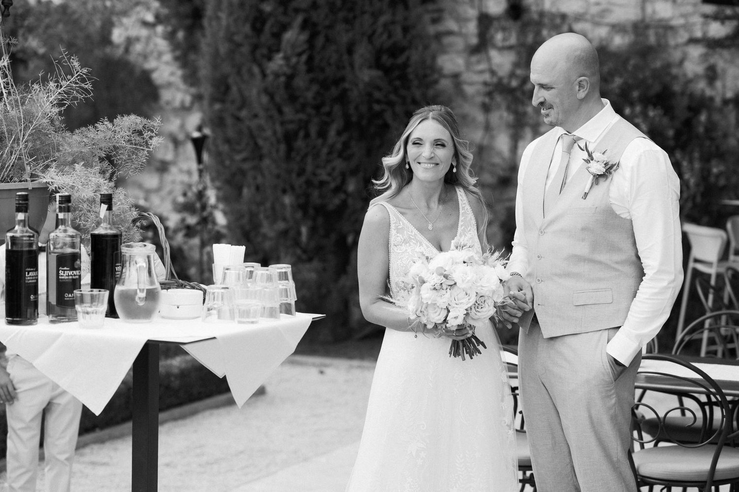 Wedding couple poses outdoors for black and white photo with reception tables in background.