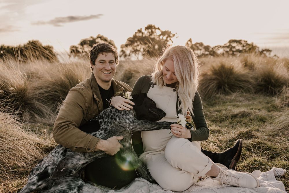 Expecting couple sitting in field of tall grass during golden hour.