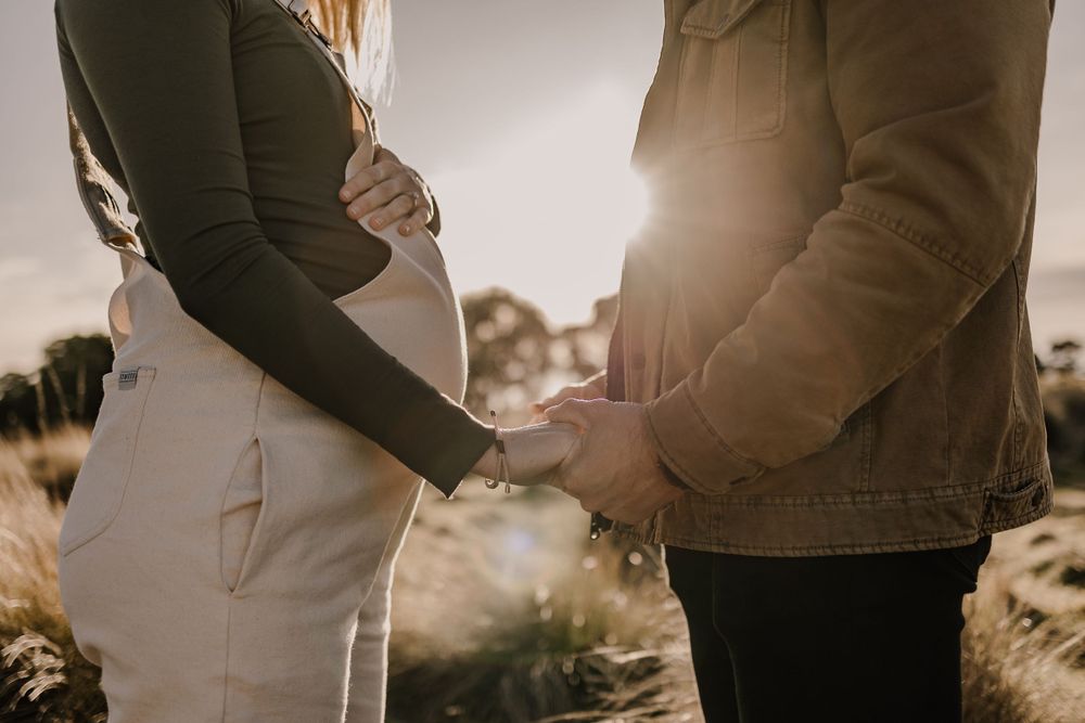 Silhouette of expecting couple holding hands over pregnant belly at sunset.